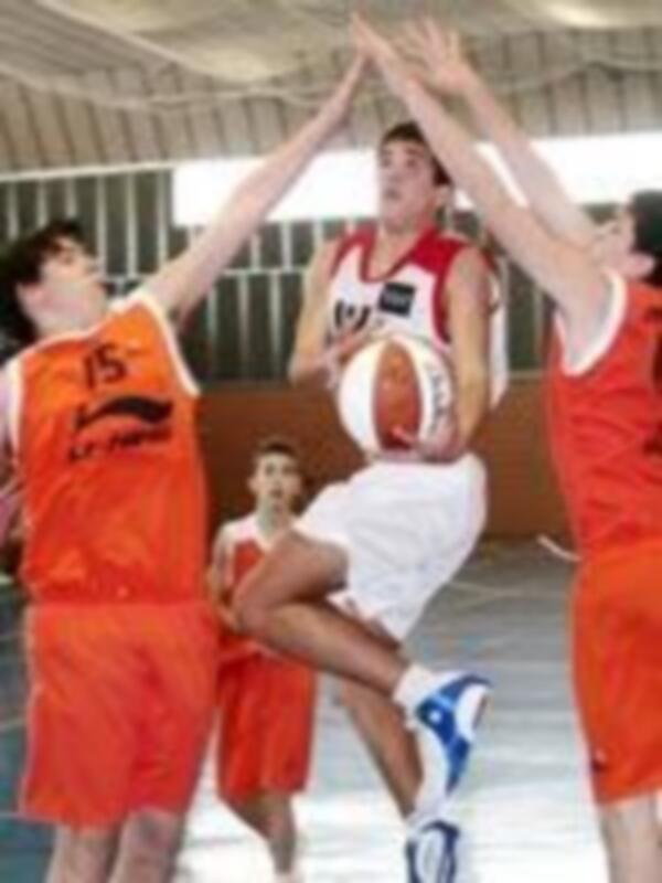 Un partido de baloncesto en un campo de juego, con jugadores en acción y una portería visible en el fondo.