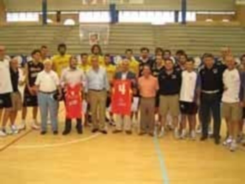 Una imagen de un grupo de personas posando en una cancha de baloncesto. La mayoría son jóvenes, algunos con camisetas y pantalones cortos deportivos, posando frente a una cancha de baloncesto con un fondo de pareds y una reja.