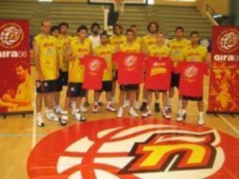 Equipo de baloncesto posando en el piso del estadio, con camisetas amarillas y shorts rojos. Logotipo de la liga en el fondo.