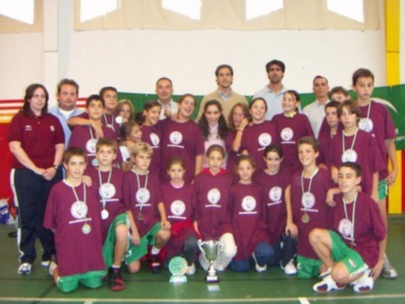 Una escuela de fútbol infantil muestra a sus jugadores con medallas y trofeos, posando en un gimnasio.