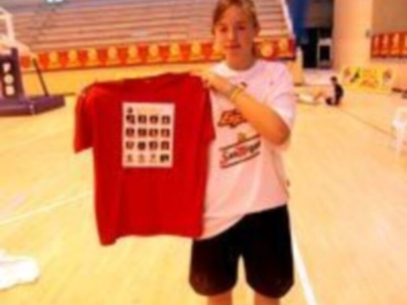 Un niño sostiene una camiseta roja con un patrón de cuadros blancos, posiblemente en una cancha deportiva.