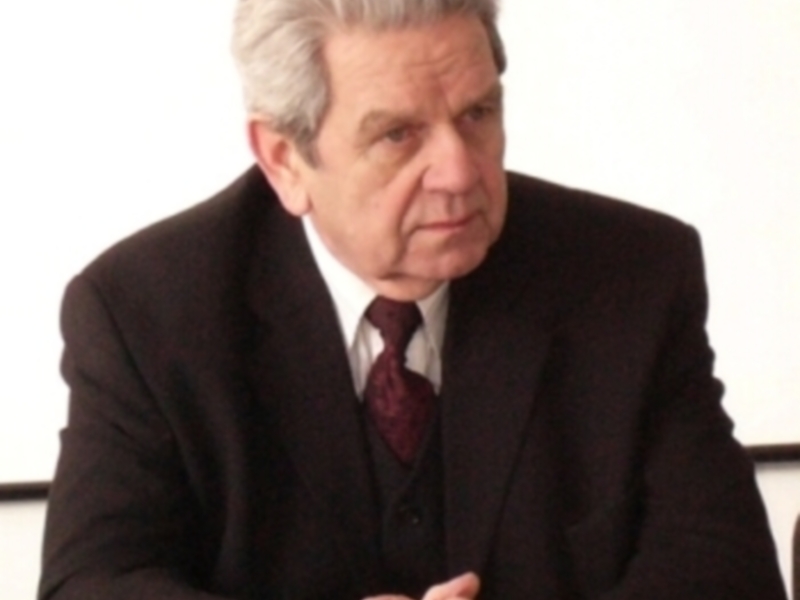 Un hombre en traje oscuro y corbata roja, con cabello gris, mirando hacia la izquierda.