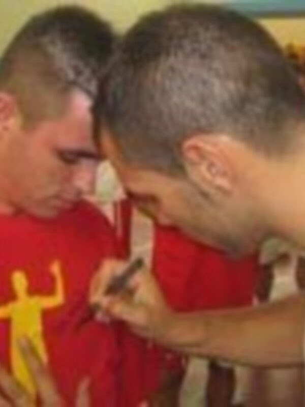 Dos jóvenes se miran en un espejo, uno con una camiseta roja y el otro con una camiseta azul, en un ambiente casual.