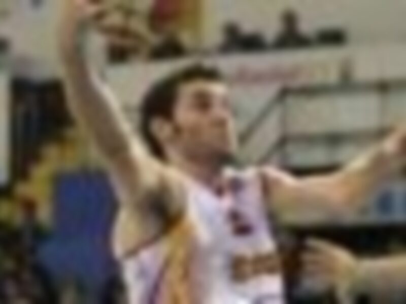 Un jugador de baloncesto en acción, con una camiseta roja y amarilla, sostiene el balón mientras realiza un tiro libre.