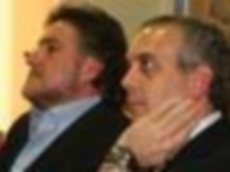 Dos personas hablando en una reunión o conferencia, con microfones en la mano.