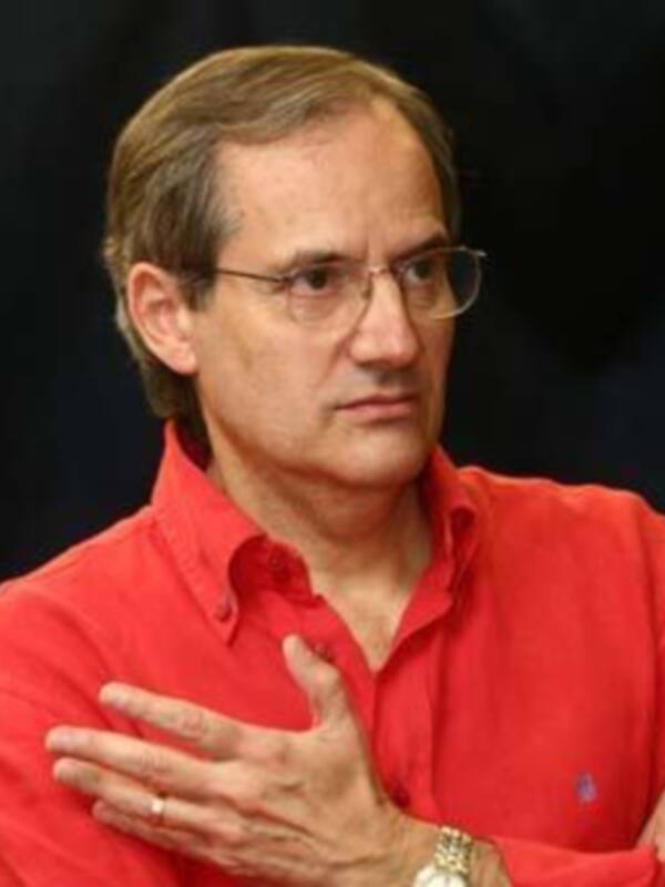 Persona con camisa roja y gafas, con las manos entrelazadas en un gesto reflexivo.