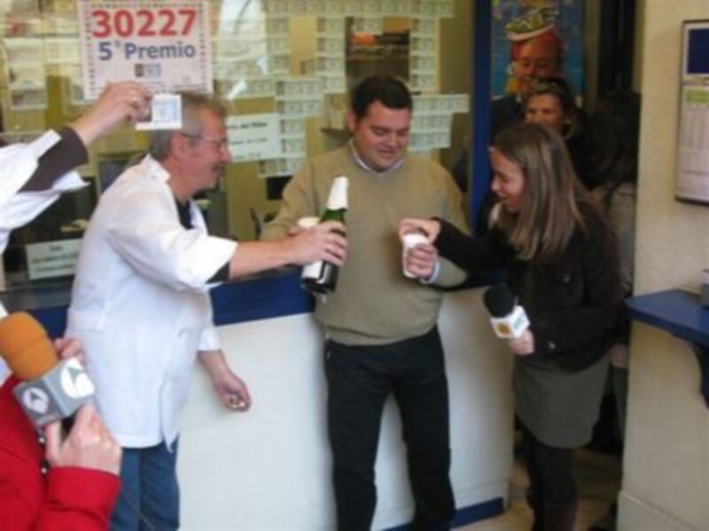 Una persona sostiene un premio mientras otros observan en una tienda de lotería.