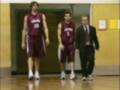 Tres personas en un gimnasio: dos jugadores de baloncesto con uniformes rojos y una persona en traje.