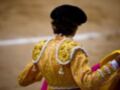 Un torero en traje tradicional, con un fondo de arena y una línea blanca que parece ser el límite del ruedo.