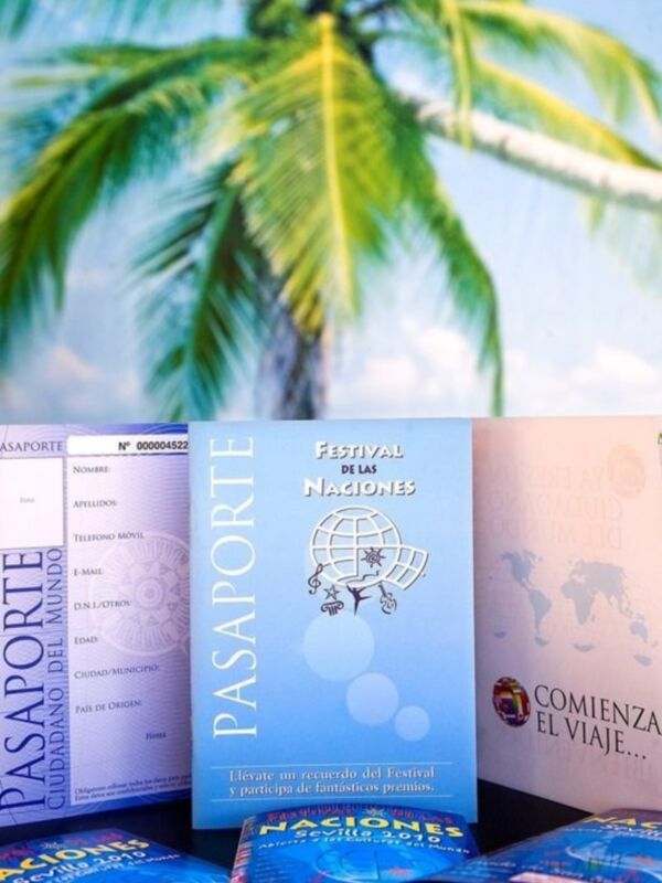 Pasaportes con información turística y promociones para el Festival de las Naciones, frente a un fondo de palmeras.