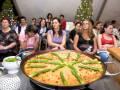 Una paella con espárragos en un recipiente de aluminio, rodeada por una audiencia.