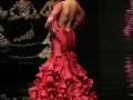 Una mujer en un vestido flamenco rojo con volantes y una gorro de plumas, posa en un escenario. Detrás, otra mujer con vestido blanco y negro también posa.