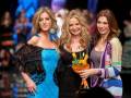 Tres mujeres posan en la pasarela de una moda, sonrientes y con vestidos elegantes. La imagen captura un momento de glamour y estilo en el mundo del fashion show.