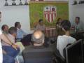 Grupo de personas reunidas en una sala con una bandera del Club Atlético Lora en el fondo.