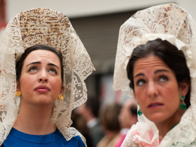 Dos mujeres con mantoncillos de encaje blanco, mirando hacia arriba y a un lado.
