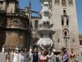 Un grupo de personas posa frente a la Mezquita-Catedral de Córdoba, con una torre en el fondo. La imagen muestra a una mujer vestida de blanco y otra de amarillo, entre otros modelos. La escena está iluminada por el sol y se puede ver una farola en primer plano.