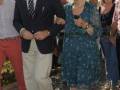 Una pareja caminando juntos, la mujer con un vestido azul con lunares y el hombre con un traje negro y pantalones beige.