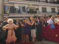 Fiesta flamenca con mujer bailando flamenco en el centro, rodeada por espectadores y fotógrafos en una plaza urbana.