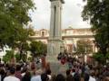 Reunión pública en plaza con estatua central y edificio histórico al fondo.