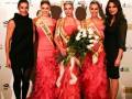 Una mujer vestida de negro y otra con un vestido rojo largo posan junto a tres mujeres también vestidas de negro, todas ellas con coronas y cintas. La imagen parece ser del certamen de belleza "Dama de España 2013" en Barcelona.