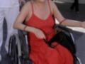 Mujer en silla de ruedas con vestido rojo, acompañada por personal médico en un entorno urbano.