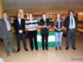 Una imagen de una competición de bowling en un centro recreativo. Se ven cinco personas, cuatro hombres y una mujer, celebrando posando en la cancha de bowling. La imagen está firmada por Tony Linares.