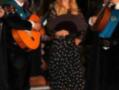 Una mujer vestida con un vestido negro y blanco a lunares, posa junto a músicos que tocan guitarra y acordeón.
