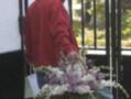 Un hombre en una chaqueta roja lleva un gran cesto de flores, incluyendo liliums y orquídeas, frente a una puerta de hierro forjado.