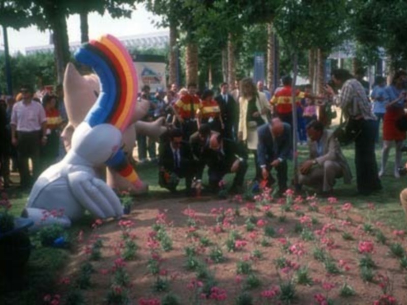 Ceremonia de plantación de flores en un evento público, con personas observando y participando.