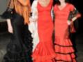 Tres mujeres vestidas con trajes de flamenca posan juntas en una fiesta nocturna.