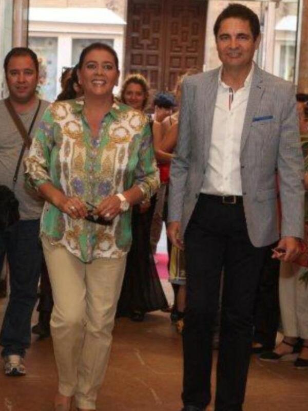 Personas en un evento formal, con una mujer en el centro luciendo un vestido floral y pantalones beige.