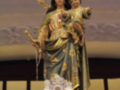Estatua dorada de la Virgen María con Niño Jesús, rodeada por flores y un círculo dorado.