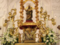 Altar con estatua central dorada, candelabros y flores blancas.