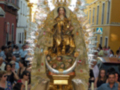 Imagen de una procesión religiosa con una imagen de la Virgen en el centro, rodeada por personas y decoraciones florales.