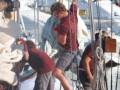 Personnel working on a ship's rigging in a marina setting.