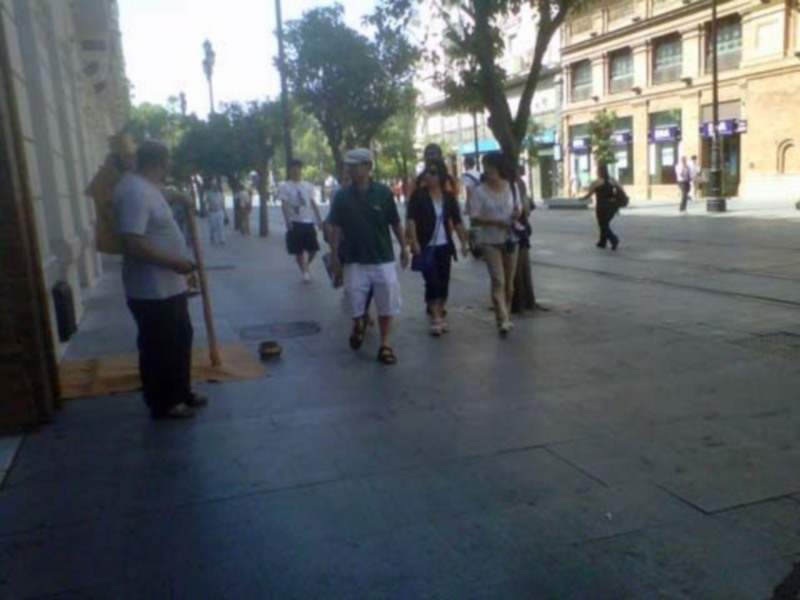 Paseo en la ciudad con personas caminando y un hombre tocando una flauta en el fondo.