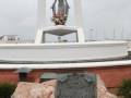 Monumento dedicado a los héroes de la independencia, ubicado en un puerto deportivo. La estatua central representa a una figura con un traje formal, rodeada por flores. En la base del monumento hay una placa con el nombre "Ricohourano".