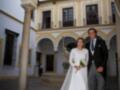 Boda en un palacio histórico con arcos y columnas. La novia lleva un vestido blanco largo, el novio una chaqueta negra y pantalones grises.