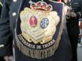 Este pié de foto muestra un uniforme militar con detalles dorados y una insignia central que incluye un escudo heráldico. La inscripción en la parte inferior del uniforme dice "MILITAR DE TIRIANA" y contiene otros detalles que no se pueden leer claramente.