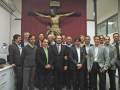 Un grupo de hombres posa frente a una imagen religiosa en un ambiente formal.