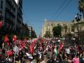 Una multitud en una manifestación con banderas y carteles, frente a un edificio histórico.