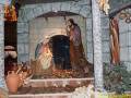 Escena navideña con María, José y el Niño Jesús en un pesebre. Detalles como la estrella de Belén, las ovejas y el arco de piedra. Decoración navideña con guirnaldas y adornos en la pared.