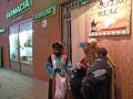 Personajes vestidos de los Reyes Magos saludan a un niño en una calle urbana frente a una farmacia.