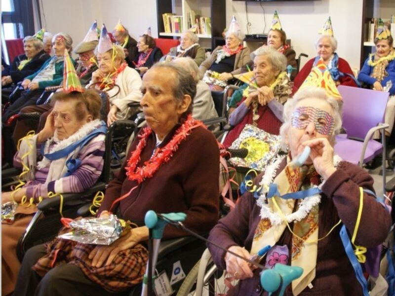 Celebración festiva con adultos mayores en sillas de ruedas, disfrutando de adornos y globos.