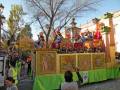 Una carroza festiva con figuras de juguetes y banderas, rodeada por espectadores en un ambiente festivo.