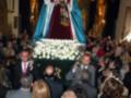 Una procesión religiosa con una imagen de un santo vestida de blanco y azul, rodeada de fieles en una iglesia.