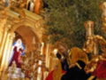 Procesión religiosa con imágenes de la Virgen y Jesús en un trono ornado con oro y telas rojas y doradas.