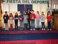 Niños y niñas en un escenario con trofeos, celebrando la Fiesta del Deporte.