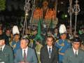Procesión religiosa con imágenes procesionales y uniformes militares en una noche iluminada.