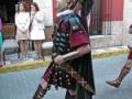Recreación histórica de soldado romano en una calle urbana, vestimenta y armadura bien detalladas.